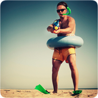 man on beach in rubber ring and holding up a water shooter